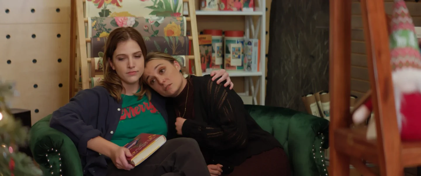Two women cuddling, while one holds a book.