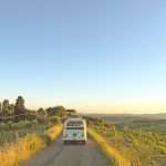 white van traveling on rough road in between green grass during sunset