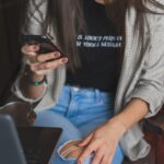 woman in white cardigan holding black smartphone
