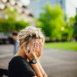 person covering face with hands outdoors
