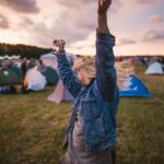 a woman raising her arms in the air in front of tents