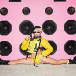 Daisy Doris May as Häns Off doing the splits in front of pink speaker