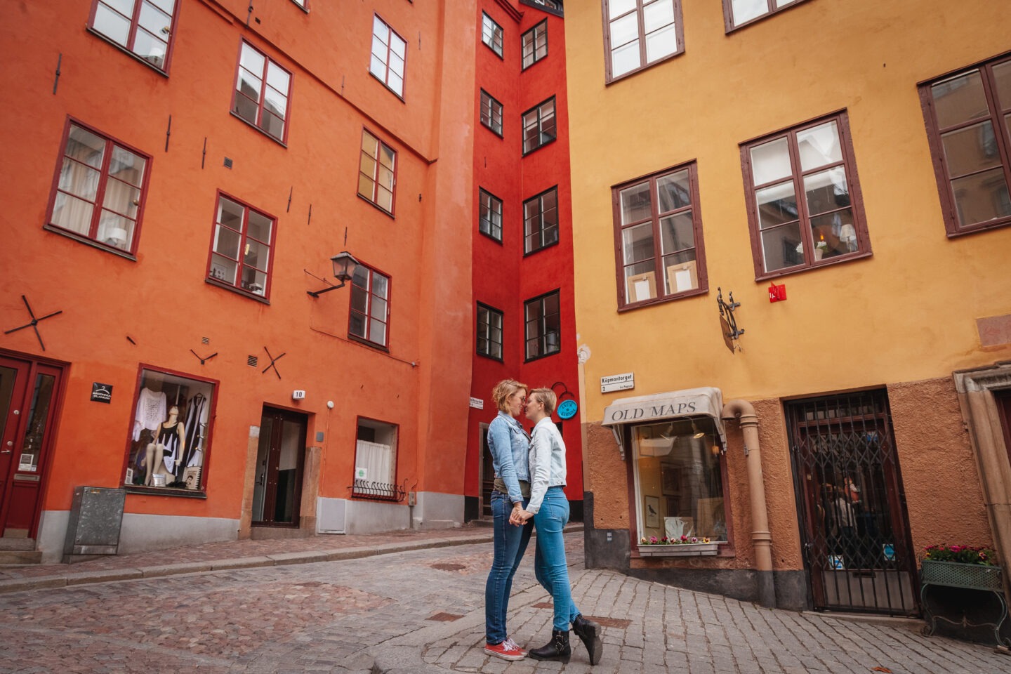 two women about to kiss near a red building