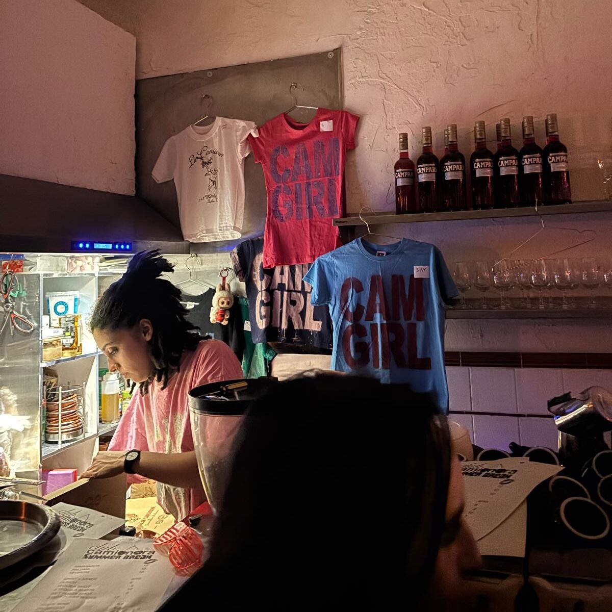 a person working behind the bar and t-shirts for sale behind.