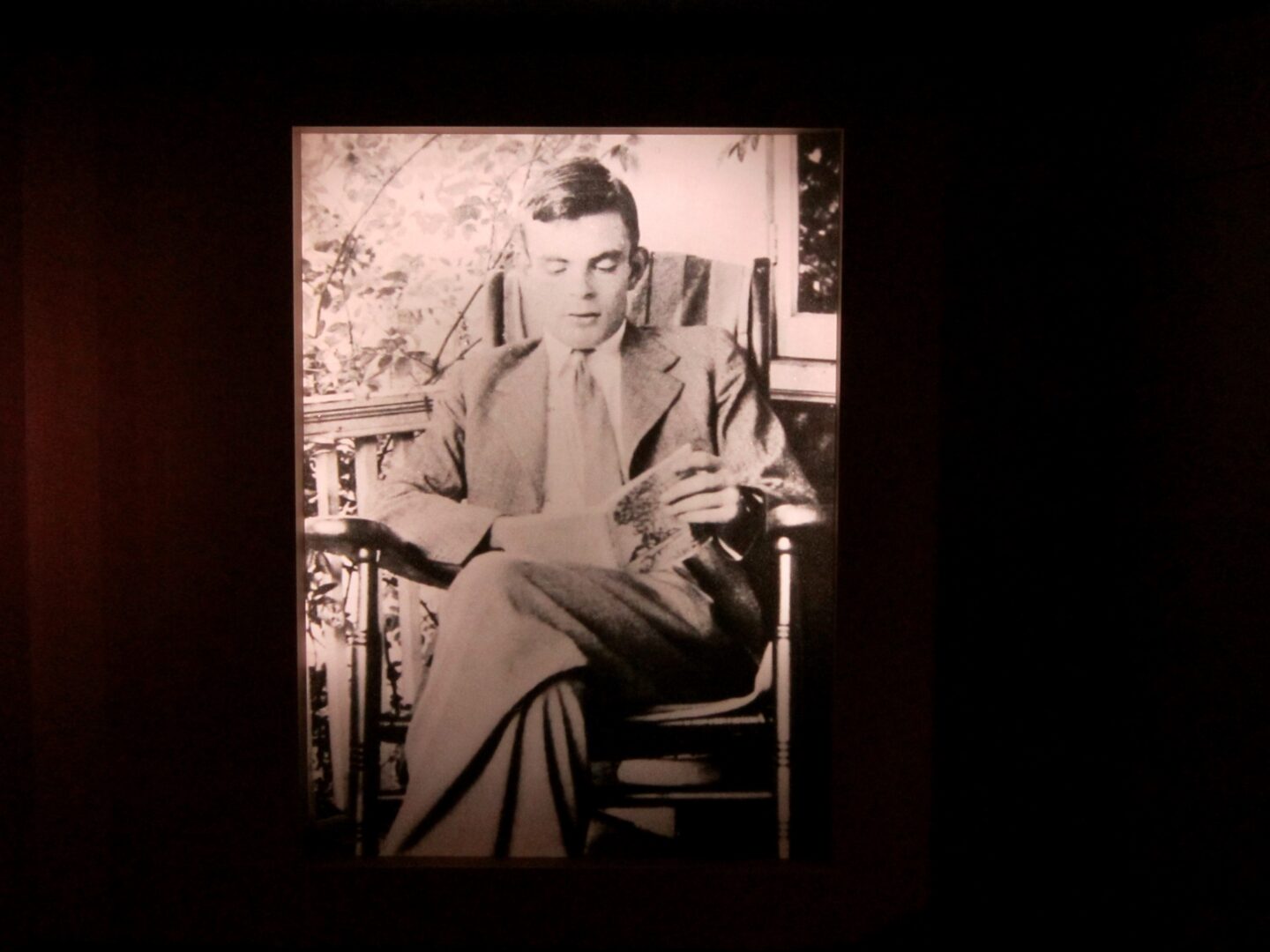 Alan Turing sitting in a chair reading a book.