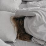 a woman is hiding under a blanket on a bed