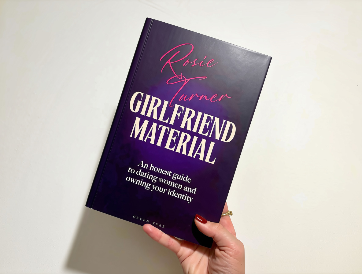 A hand holds up a copy of Girlfriend Material, the novel