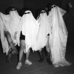 Four individuals dressed as playful ghosts, showcasing Halloween spirit and creativity under dim lighting.